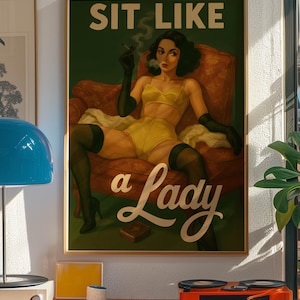 May include: A framed vintage-style poster with the text "SIT LIKE a Lady." The artwork depicts a woman in yellow lingerie, black gloves, and stockings, smoking a cigarette while seated in a red armchair. The poster is in a gold frame.