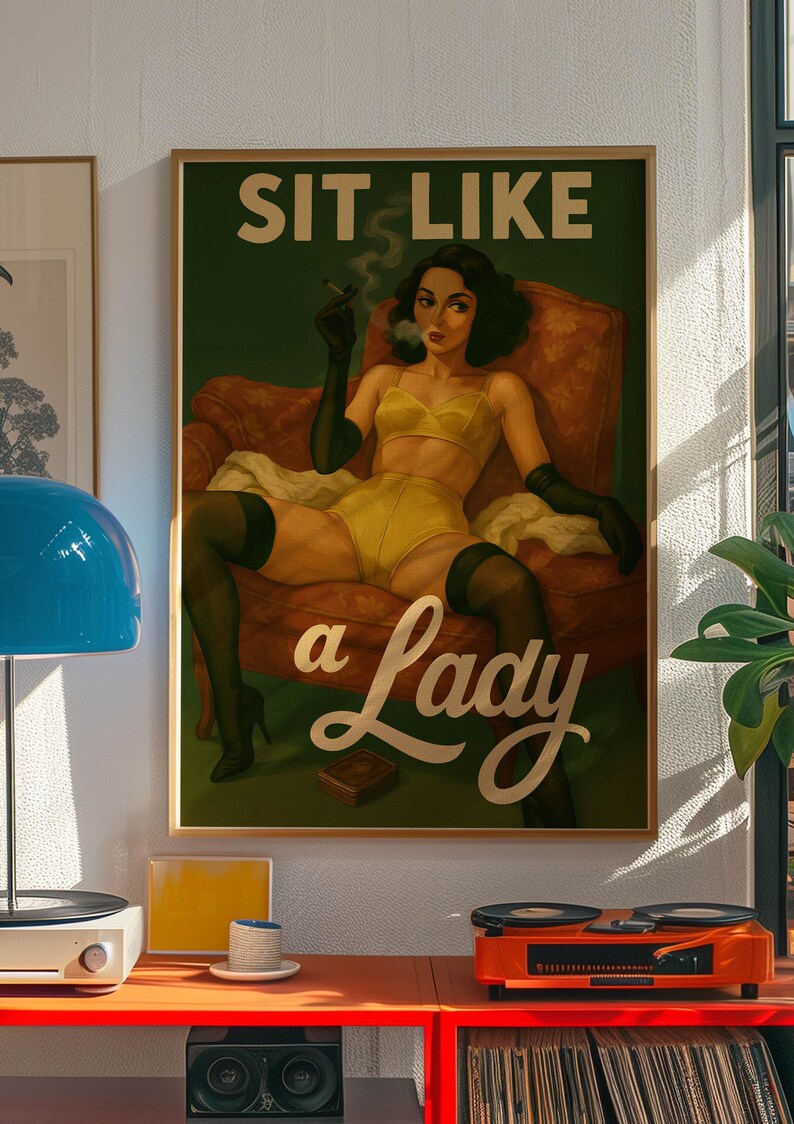 May include: A framed vintage-style poster with the text "SIT LIKE a Lady." The artwork depicts a woman in yellow lingerie, black gloves, and stockings, smoking a cigarette while seated in a red armchair. The poster is in a gold frame.