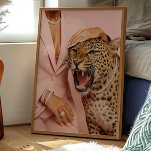May include: Framed art print featuring a pink suit, a roaring leopard, and diamond jewelry. The artwork includes a diamond necklace, bracelets, and rings. The leopard has a diamond necklace. The frame is made of wood.