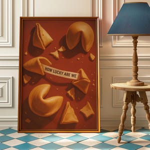 Könnte beinhalten: Ein gerahmtes Kunstwerk mit Glückskeksen, von denen einige zerbrochen sind, auf einem rotbraunen Hintergrund. Ein Keks zeigt die Botschaft: „HOW LUCKY ARE WE“. Das Kunstwerk befindet sich in einem goldenen Rahmen und lehnt an einer Wand.