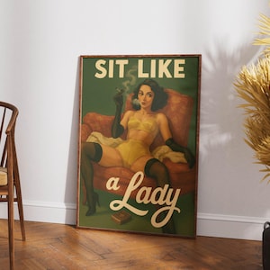 May include: A framed vintage-style poster with the text "SIT LIKE a Lady." The artwork depicts a woman in yellow lingerie, black gloves, and stockings, seated in a red armchair, smoking a cigarette. The background is green.