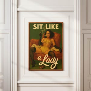 May include: A framed vintage-style print featuring a woman in yellow lingerie, black gloves, and stockings, seated in a red armchair. The print has the text "SIT LIKE a Lady" in a retro font against a green background.