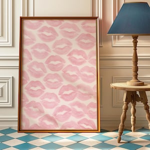 May include: A framed artwork featuring a pattern of pink lipstick kiss prints on a cream background. The artwork is in a gold-colored frame and leans against a white wall. The floor has a blue and white checkered pattern.