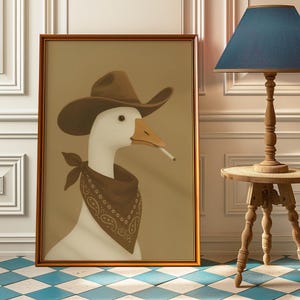 Op de afbeelding: Ingelijste kunstwerk met een witte gans met een bruine cowboyhoed en bandana, met een sigaret in de bek. Het kunstwerk heeft een sepia-achtergrond en een goudkleurige lijst. De gans is het centrale onderwerp van de afbeelding.