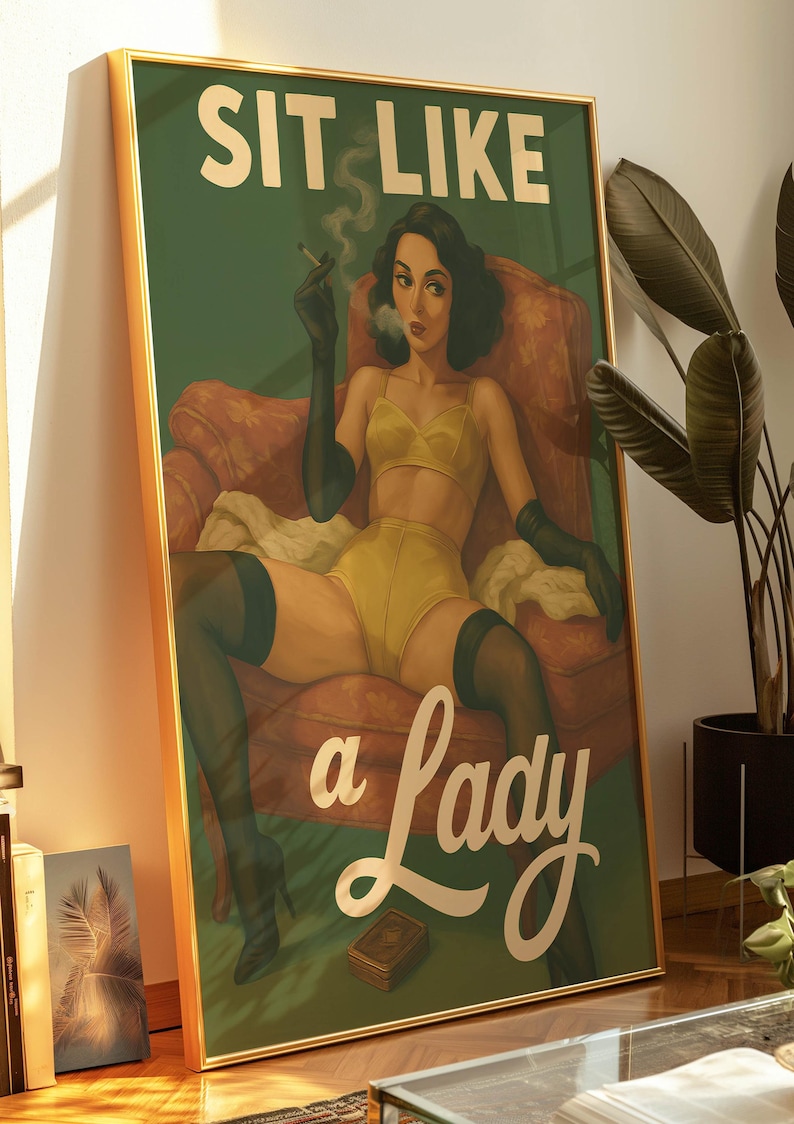 May include: Framed vintage-style poster with a woman in yellow lingerie, black gloves, and stockings, smoking a cigarette while seated in a red armchair. The text "SIT LIKE a Lady" is displayed in gold lettering on a green background.