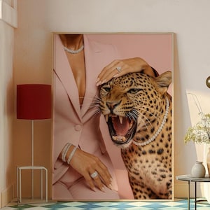 May include: A framed artwork featuring a roaring leopard wearing a diamond necklace, with a woman in a pink suit and diamond jewelry. The leopard's fur is spotted, and the woman's hand rests on its head. The background is a soft pink.