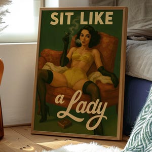 May include: Framed vintage-style poster with the text "SIT LIKE a Lady." The artwork depicts a woman in yellow lingerie, black gloves, and stockings, smoking a cigarette while seated in a red armchair. The poster is in a wooden frame.