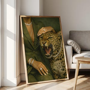 May include: A framed art print featuring a woman in a green suit with diamond jewelry, posing with a snarling leopard wearing a diamond necklace. The artwork is set against a green backdrop, with a wooden frame.
