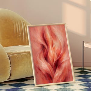 May include: A framed abstract art print with a flowing, flame-like design in red and peach hues. The artwork is displayed on a blue and white diamond patterned rug, leaning against a yellow velvet armchair.