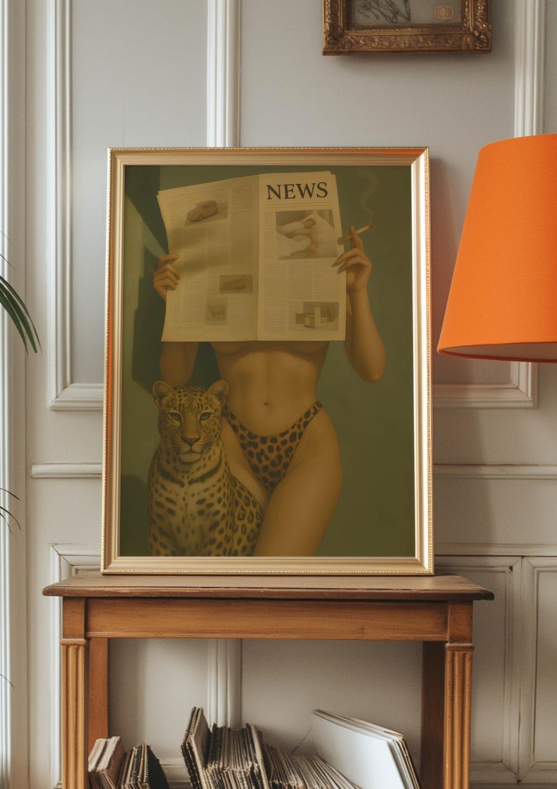 May include: Framed artwork featuring a woman holding a newspaper with the headline "NEWS", a leopard, and a cigarette. The woman wears leopard print underwear. The artwork is in a gold frame and sits on a wooden table.