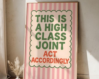 May include: A framed poster with a pink and white striped background. The poster features the text "THIS IS A HIGH CLASS JOINT ACT ACCORDINGLY" in green and red, within a scalloped border. The frame is a light brown color.