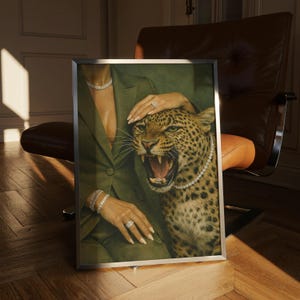 May include: A framed artwork featuring a woman in a green suit with diamond jewelry, and a snarling leopard wearing a diamond necklace. The artwork is set against a backdrop of a brown leather chair and a wooden floor.