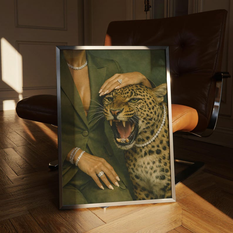 May include: A framed artwork featuring a woman in a green suit with diamond jewelry, and a snarling leopard wearing a diamond necklace. The artwork is set against a backdrop of a brown leather chair and a wooden floor.