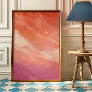 May include: Framed art print depicting a sunset sky with orange, pink, and white clouds. A crescent moon is visible. The artwork is in a gold frame. The print is displayed indoors.
