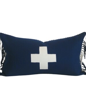 May include: A blue and white throw pillow with a white cross design and fringe trim.