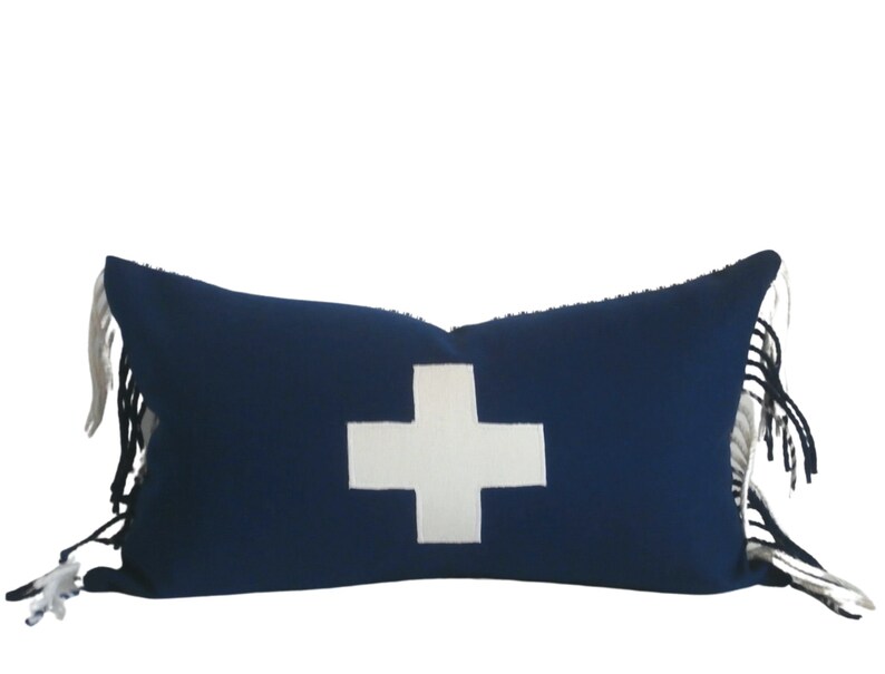 May include: A blue and white throw pillow with a white cross design and fringe trim.