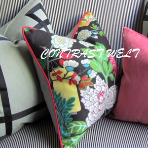 May include: Three decorative throw pillows with a black and white striped background. The pillows are black with a floral pattern in shades of red, green, white, and yellow. The pillow in the foreground has a red trim. The pillow in the background is a solid pink.