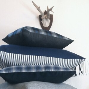 May include: Three blue and white patterned throw pillows with fringe. The top pillow has a plaid pattern, the middle pillow has a striped pattern, and the bottom pillow has a plaid pattern.