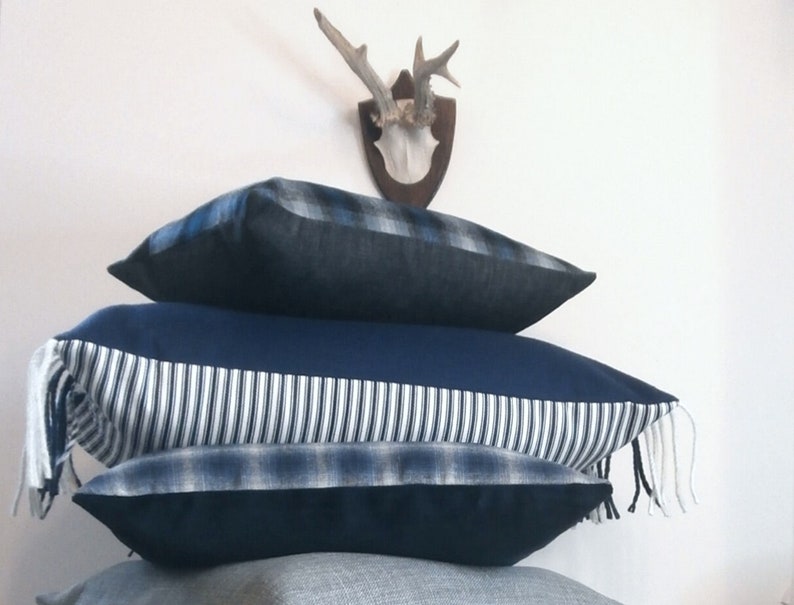May include: Three blue and white patterned throw pillows with fringe. The top pillow has a plaid pattern, the middle pillow has a striped pattern, and the bottom pillow has a plaid pattern.