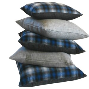 May include: A stack of five decorative throw pillows. The bottom pillow has a blue and black plaid pattern. The next pillow is a solid grey. The third pillow has a blue and black plaid pattern. The fourth pillow is a solid grey. The top pillow has a blue and black plaid pattern.