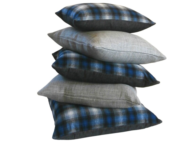 May include: A stack of five decorative throw pillows. The bottom pillow has a blue and black plaid pattern. The next pillow is a solid grey. The third pillow has a blue and black plaid pattern. The fourth pillow is a solid grey. The top pillow has a blue and black plaid pattern.