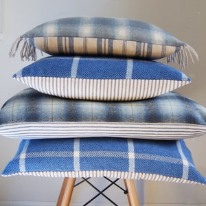 Puede incluir: Cuatro almohadas de tiro de cuadros azules y blancos apiladas en una silla de madera. Las almohadas tienen un ribete blanco y azul a rayas.