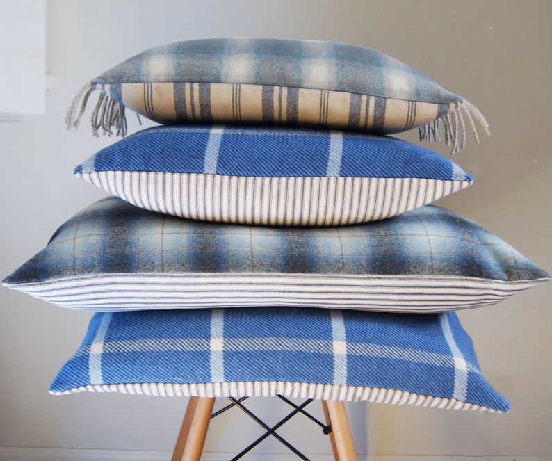 Puede incluir: Cuatro almohadas de tiro de cuadros azules y blancos apiladas en una silla de madera. Las almohadas tienen un ribete blanco y azul a rayas.
