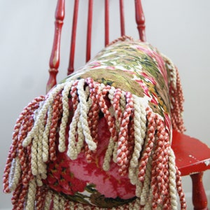 May include: A red wooden chair with a floral patterned pillow with a fringe trim. The pillow is made of a soft fabric and has a white and red fringe.