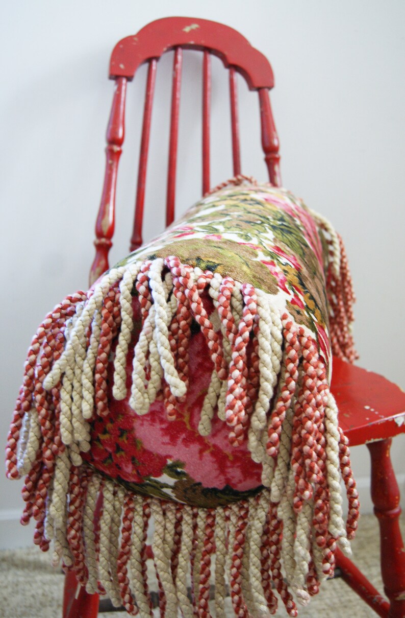 May include: A red wooden chair with a floral patterned pillow with a fringe trim. The pillow is made of a soft fabric and has a white and red fringe.
