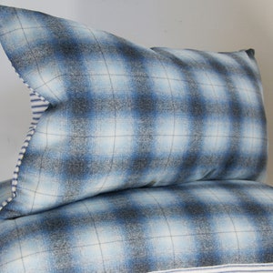 Puede incluir: Dos almohadas de sof&aacute; de cuadros azules y blancos con ribete blanco y azul a rayas.