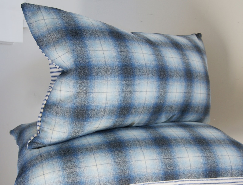 Puede incluir: Dos almohadas de sof&aacute; de cuadros azules y blancos con ribete blanco y azul a rayas.
