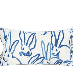 May include: A white rectangular pillow with a blue and white striped border. The pillow features a repeating pattern of blue bunny silhouettes.