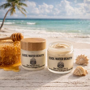 May include: Two jars of Cool Water Beauty balm with wooden lids and labels that read "Bee Venom 2% & Sea Buckthorn Collagen Boost Balm." The jars sit on a white surface with seashells, honey, and a honeycomb. The background shows a beach and ocean.