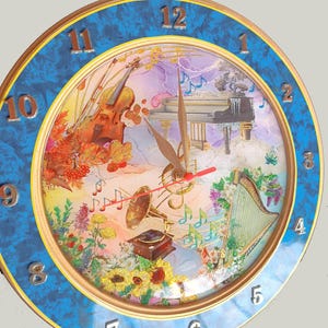 Puede incluir: Un reloj redondo azul y dorado con instrumentos musicales y notas en la esfera. El reloj tiene números romanos para las horas y una aguja de segundos roja.