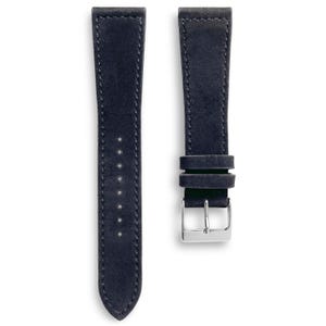 May include: Two navy blue watch straps with a suede-like texture. The straps are stitched along the edges with a lighter thread. One strap has a silver-colored buckle. The straps are designed to attach to a watch.