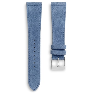 May include: Two-piece light blue suede watch strap with a silver-colored buckle. The strap has a stitched design and several holes for adjustment. The suede material has a soft, textured appearance.