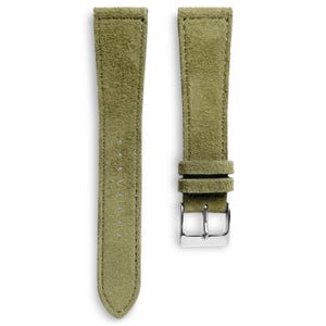 May include: Two-piece olive green suede watch strap with a silver-tone buckle. The strap has a soft, textured appearance and is designed for a watch. The strap is shown against a white background.