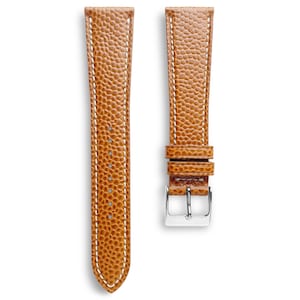 Puede incluir: Correa de reloj de dos piezas en cuero marrón claro con superficie texturizada y costuras blancas. La correa de la derecha tiene una hebilla plateada. El cuero tiene un aspecto granulado.