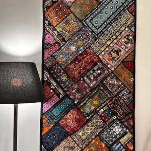 Puede incluir: Un tapiz de pared de patchwork colorido con intrincados bordados y detalles de espejo. El tapiz está hecho de varias telas en tonos de rojo, azul, verde, naranja y rosa. Presenta un patrón geométrico y está enmarcado con un borde negro.