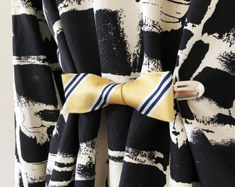 May include: A black and white patterned fabric with a yellow and blue bow tie attached with a silver clip.
