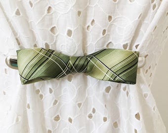 May include: A green and white plaid bow tie with a silver clip. The bow tie is tied and ready to wear.