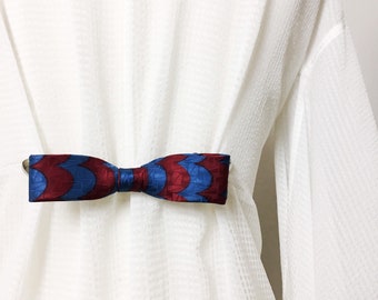 May include: A white shirt with a blue and red patterned bow tie.