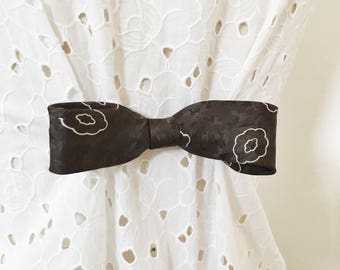 May include: A brown bow tie with a floral pattern. The bow tie is tied and is on a white background.