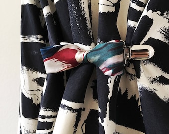 May include: A black and white patterned fabric with a colorful fabric bow tied and secured with a silver clip.
