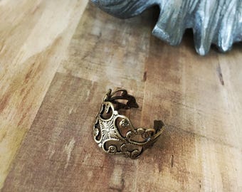 May include: A gold-toned filigree ring with a floral design. The ring is open on one side and has a delicate, intricate pattern.