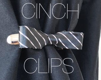 May include: A black and white striped tie bow is used as a cinch clip to hold a black fabric together. The text "CINCH CLIPS" is written in white on the black fabric. The text "@outlying" is written in pink at the bottom of the image.