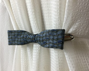 May include: A blue and green patterned bow tie curtain tieback with a silver metal clip.