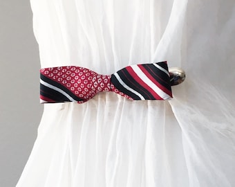 May include: A red and black patterned bow tie with a silver clip. The bow tie is made of fabric and has a geometric pattern on one side and stripes on the other.