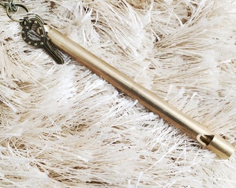 May include: A gold whistle necklace with a key charm. The whistle is a long, thin tube with a hole at one end. The key charm is a small, ornate key with a heart-shaped hole.