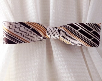 May include: A patterned bow tie in shades of brown, gold, and white. The fabric features diagonal stripes and a repeating dotted pattern. The bow tie is tied in the center and appears to be made of silk or a similar material.